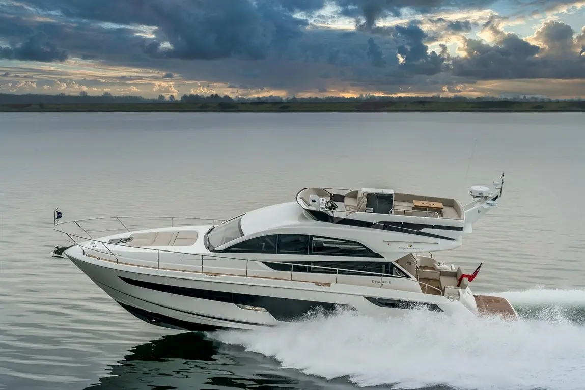 Luxury motor yacht cruising on calm waters, showcasing elegant design against a cloudy sunset sky.
